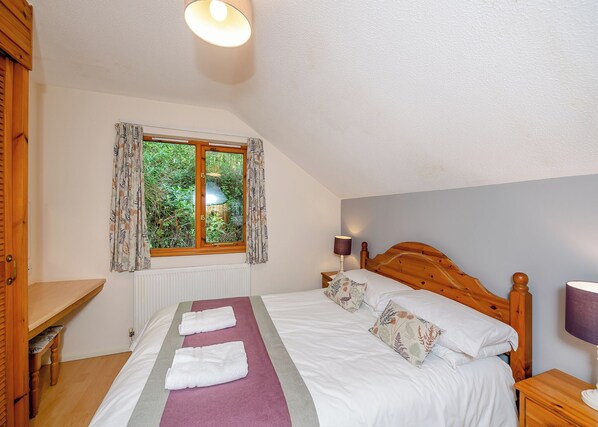 A bedroom with a bed, a window, a bedside table, and a lamp.