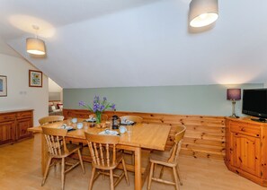 Un coin repas avec une table en bois, des chaises, un vase de fleurs et un téléviseur posé sur un meuble en bois.