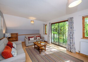Een woonkamer met een bank, een bijzettafeltje, een radiator en een groot raam met gordijnen.