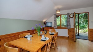 Een eetgedeelte met een houten tafel, stoelen, een bloevas, een koffiezetapparaat en een televisie.