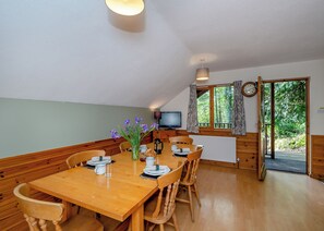 A dining area with a wooden table, chairs, a vase of flowers, a coffee maker, and a television.