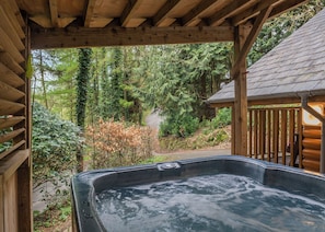 A hot tub under a wooden pergola with a forest view.