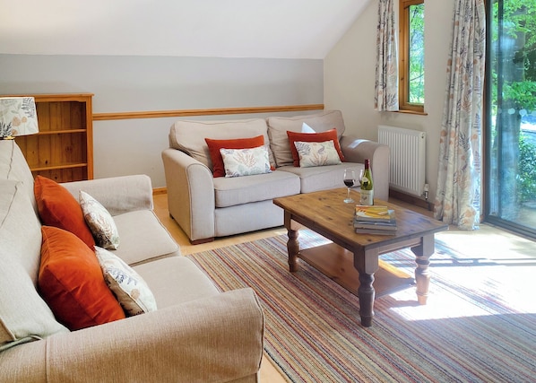 A living room with a sofa, armchair, and coffee table, a bookshelf, and a window with curtains.