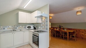 Een moderne keuken met witte kasten, een magnetron en een oven. Er is een eethoek met houten stoelen en een tafel.