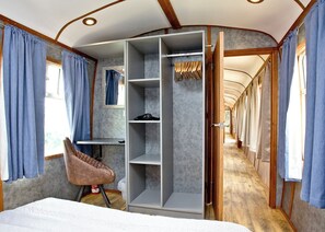 Un compartimento de tren estrecho con una cama, zona de asientos, armario y una pequeña mesa.
