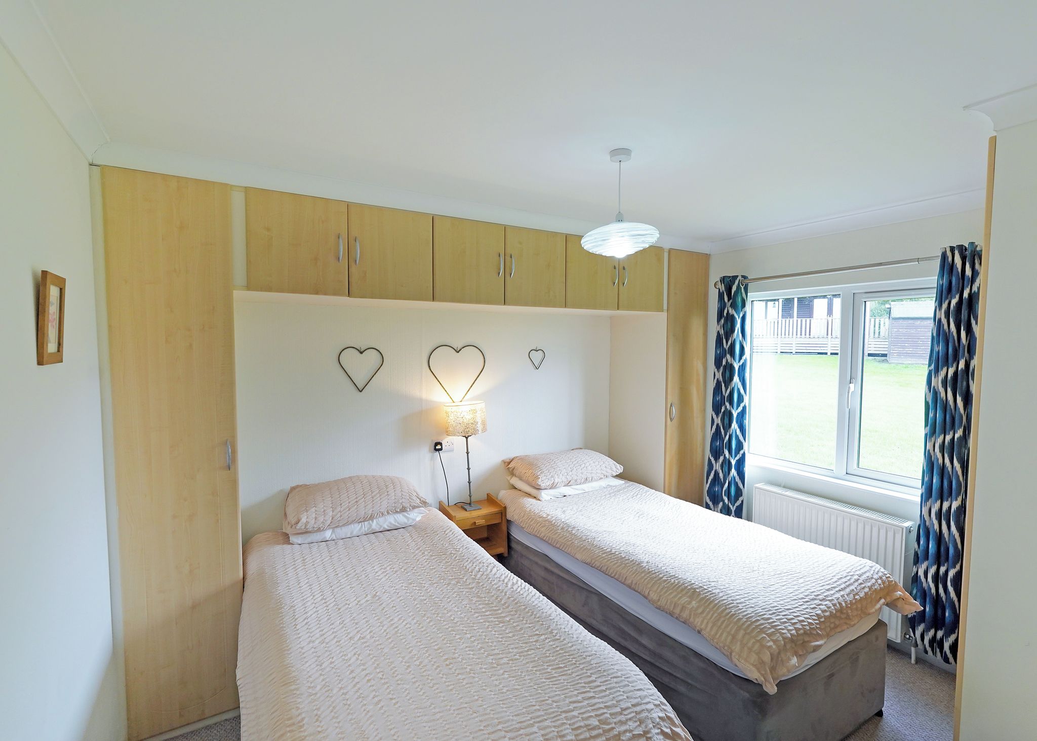 A bedroom with two beds, wooden cabinets, a ceiling light, and a window with curtains.