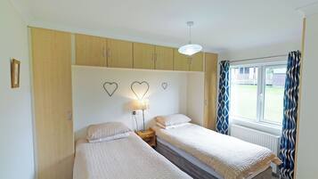 A bedroom with two beds, wooden cabinets, a ceiling light, and a window with curtains.