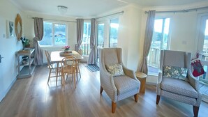 Un vaste espace de vie comprenant une table à manger, deux fauteuils et une vue sur l’extérieur grâce à de grandes fenêtres.