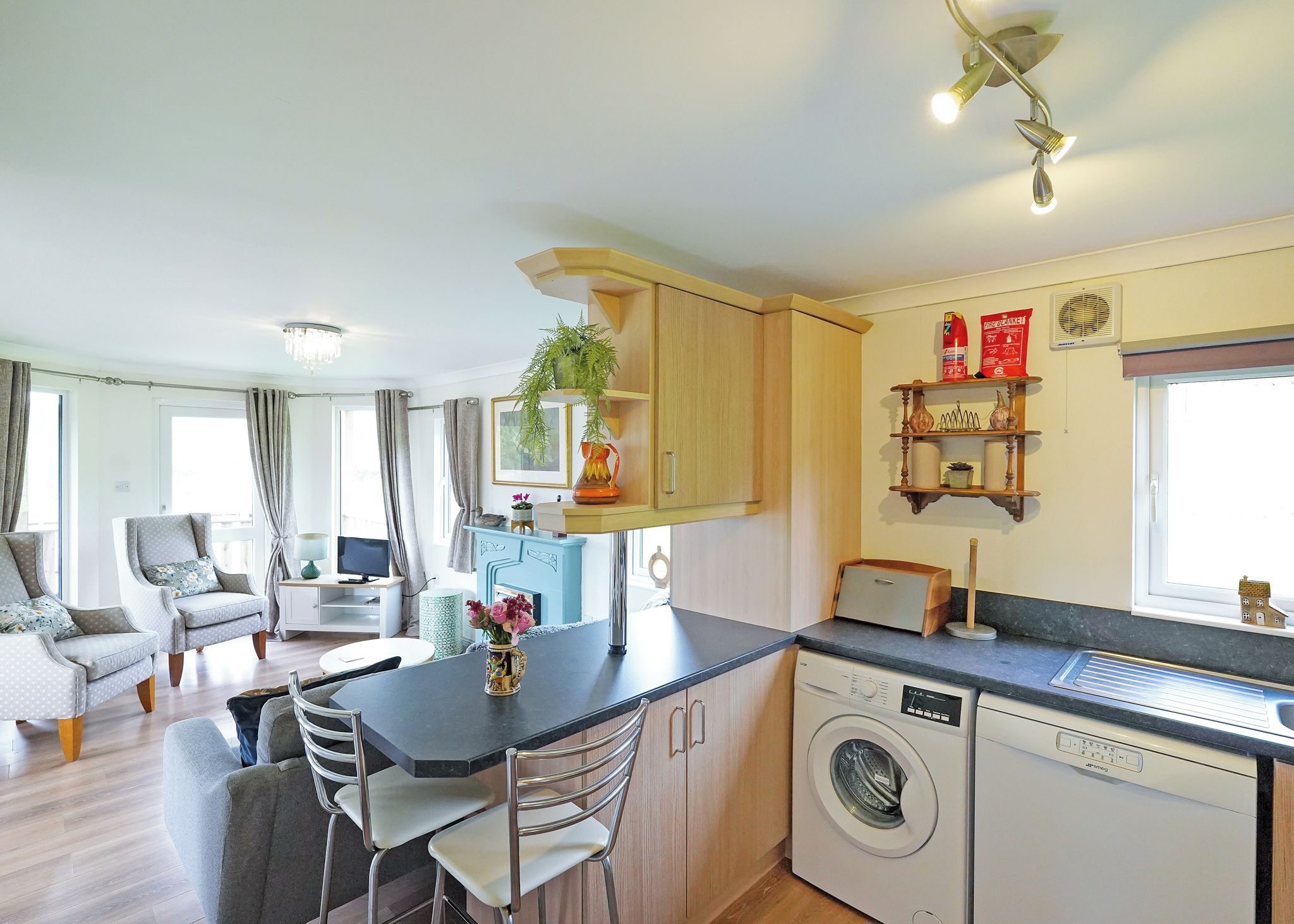 A modern kitchen with a washing machine, a dining area with a table and chairs, and a living room with a sofa and a TV.