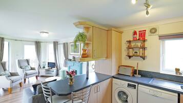 A modern kitchen with a washing machine, a dining area with a table and chairs, and a living room with a sofa and a TV.
