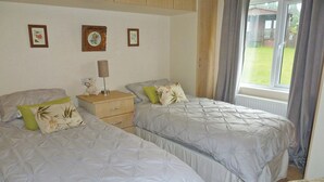 Une chambre avec deux lits, une table de chevet, une lampe et une fenêtre donnant sur l’extérieur.