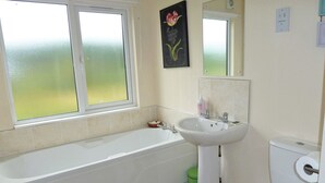 Une salle de bain équipée d’une baignoire, d’un lavabo, de toilettes et d’une fenêtre en verre dépoli.