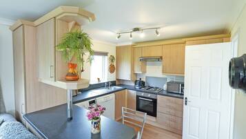 A compact kitchen with a dining area, featuring a built-in oven, microwave, and a small refrigerator.
