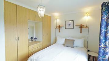 A bedroom with a bed, a wooden wardrobe, a mirror, a bedside table, and wall-mounted lights.