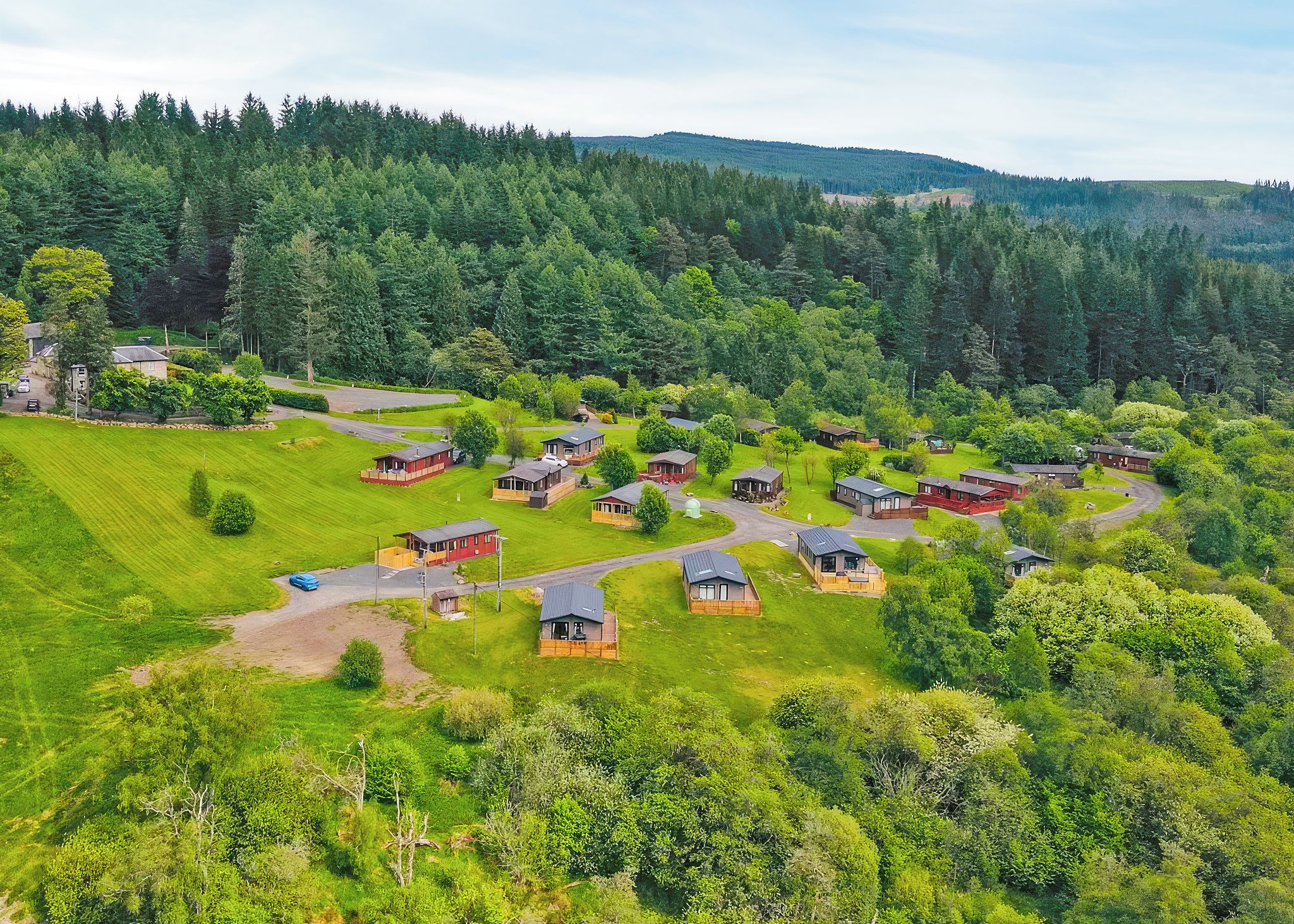 A rural area with multiple small cabins surrounded by lush greenery and a forested hill in the background.