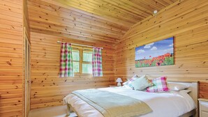 A wooden-paneled bedroom with a bed, curtains, a painting, and a nightstand. - Lodge with one king-size double with en suite bathroom with shower. (Kilcot, Newent)