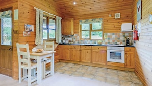 A wooden cabin kitchen with a dining table, chairs, a stove, and a window. - Lodge with one king-size double with en suite bathroom with shower. (Kilcot, Newent)