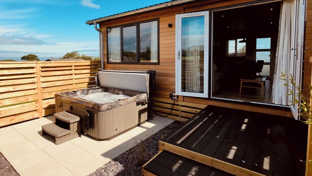 Uma cabana de madeira com banheira de hidromassagem, um alpendre e uma porta de correr que dá para o interior.