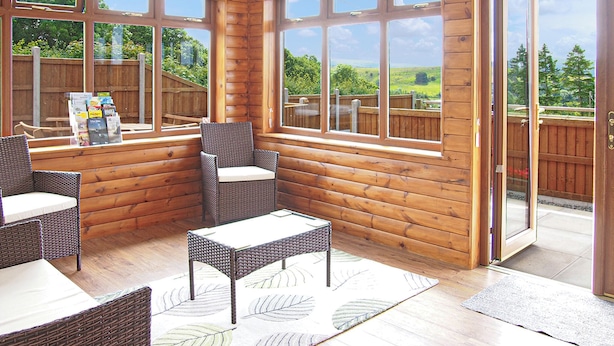 Une cabane en bois dotée d’un patio aménagé avec des meubles en osier et de grandes fenêtres.