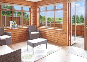 A wooden cabin with a patio area featuring wicker furniture and large windows. - Spacious lodge with one double and one twin. (Penybont, Llandrindod Wells)