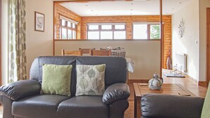 Un salon avec un canapé en cuir, une table basse en bois et une vue sur l’extérieur grâce à de grandes fenêtres.