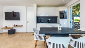 A modern kitchen with white cabinets, a dark countertop, and a built-in oven. There is a dining area with a dark table and white chairs. - Gorgeous apartment in Labin with WiFi (Labin)