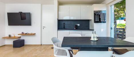 A modern kitchen with white cabinets, a dark countertop, and a built-in oven. There is a dining area with a dark table and white chairs.