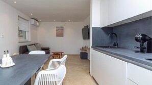 A modern kitchen with a dark countertop, white cabinets, and a black faucet. There is a dining area with a table and chairs, and a sofa in the background. - Gorgeous apartment in Labin with WiFi (Labin)