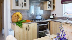 A kitchen with wooden cabinets, a gas stove, an oven, and a dining area with a table set for two. - 2 bedroom accommodation in Llanon (Llanon)