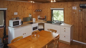 Een keuken met houten lambrisering, witte kastjes, een houten eettafel en een raam voor natuurlijk licht.