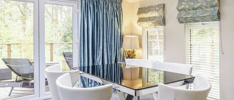 A dining area with a glass table, white chairs, a lamp, and a view of the outdoors.