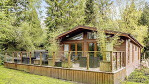 Una cabana de fusta amb terrassa, seients exteriors i un tancament de vidre.
