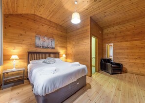 En stuga med träpanel, ett rum med en säng, två sänglampor, en tavla och en massagestol.