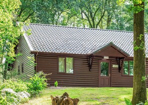 A wooden cabin with a tiled roof, surrounded by trees and greenery.
