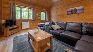 A cozy cabin interior with a wooden floor, a leather sofa, a wooden coffee table, a television on a wooden stand, and a painting on the wall. - Woodland Rowan Lodge (Ellesmere)