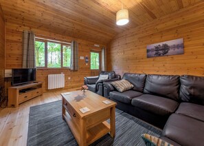 En mysig stuga med trägolv, en soffa klädd i läder, ett soffbord i trä, en tv på ett träställ och en tavla på väggen.