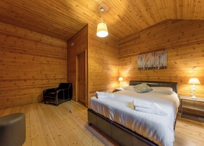 A wooden cabin room with a bed, two bedside lamps, a chair, and a painting on the wall.