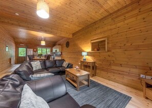 A cozy cabin interior with a leather sofa, a dining table, and a kitchen area. - Woodland Rowan Lodge (Ellesmere)