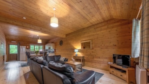 A cabin interior with a wooden interior, a sofa, a television, and a kitchen area. - Woodland Rowan Lodge (Ellesmere)