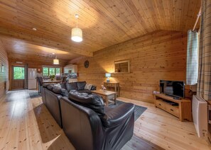 A cabin interior with a wooden interior, a sofa, a television, and a kitchen area. - Woodland Rowan Lodge (Ellesmere)
