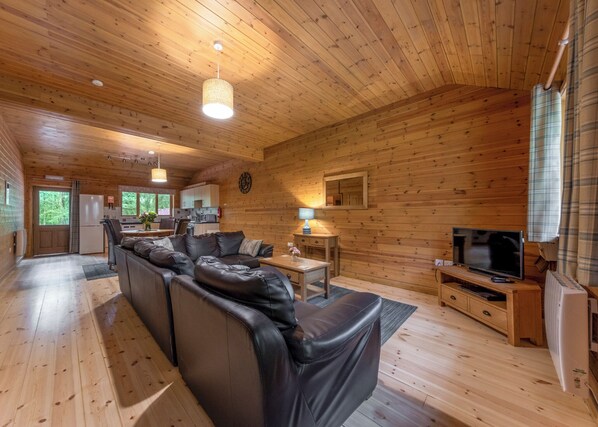 A cabin interior with a wooden interior, a sofa, a television, and a kitchen area.