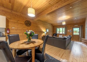 A wooden interior with a round dining table, black leather chairs, a sofa, and a television.