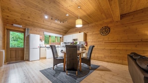 A wooden cabin interior with a dining area, kitchen, and a large window. - Woodland Rowan Lodge (Ellesmere)