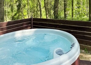 A hot tub with a wooden deck and a forest backdrop.