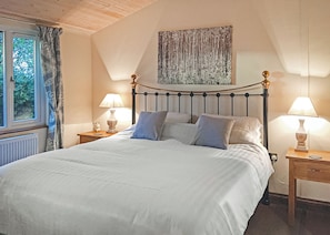 Uma cama bem arrumada com lençóis brancos, duas mesas de cabeceira com abajures, uma janela com cortinas e um quadro na parede.