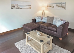 Uma sala de estar com um sofá marrom, uma mesa de centro de madeira e duas pinturas na parede.