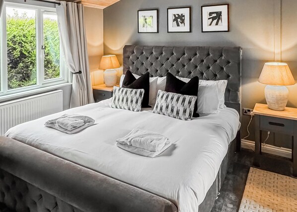 Une chambre d’hôtel avec un grand lit, deux lampes de chevet, une tête de lit grise et trois tableaux encadrés accrochés au mur.