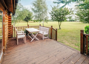 A wooden deck with a table and two chairs, overlooking a grassy area with trees. - One double with en suite shower and one twin. (Laxfield, Nr Woodbridge)