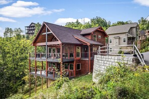Een houten vakantiehuis met meerdere verdiepingen en een balkon, omgeven door weelderige begroeiing.