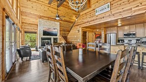 A wooden cabin interior with a dining area, kitchen, and fireplace.